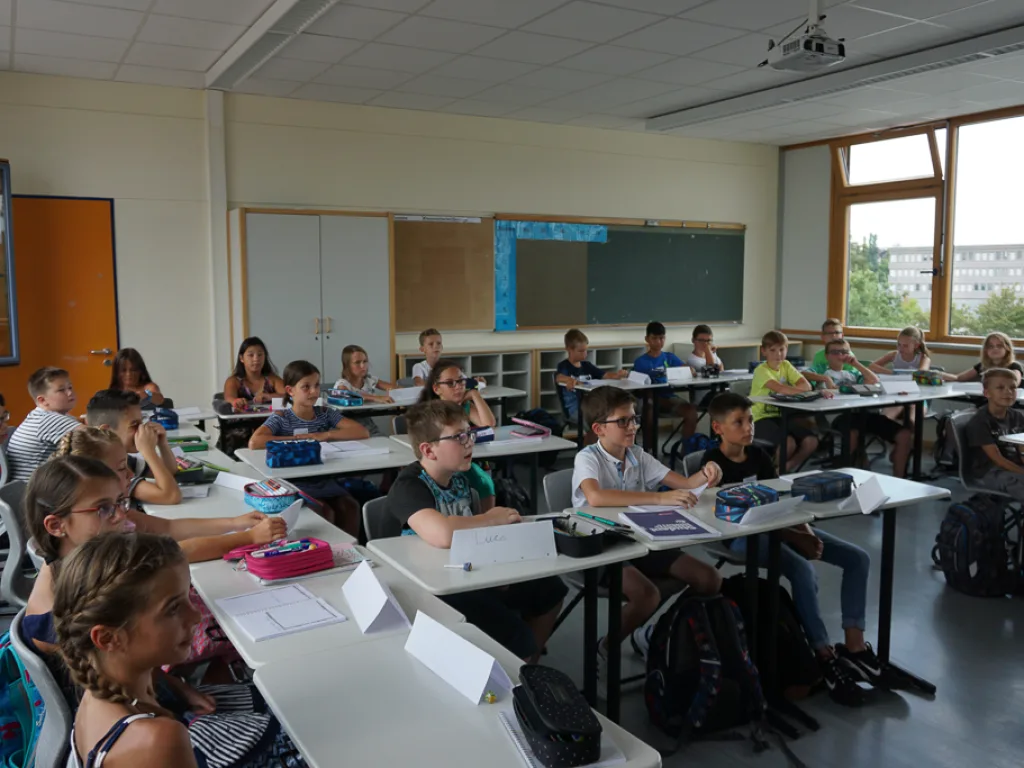 Kinder sitzen an Gruppentischen im Klassenraum.